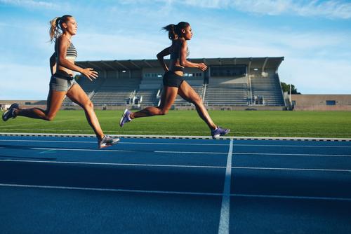 Two young women running on a blue track.