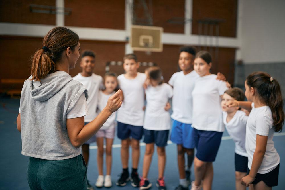 Female physical education teacher talking to girls and boys in gym.