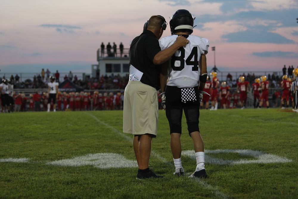 A coach talking to a young male football player on the field.