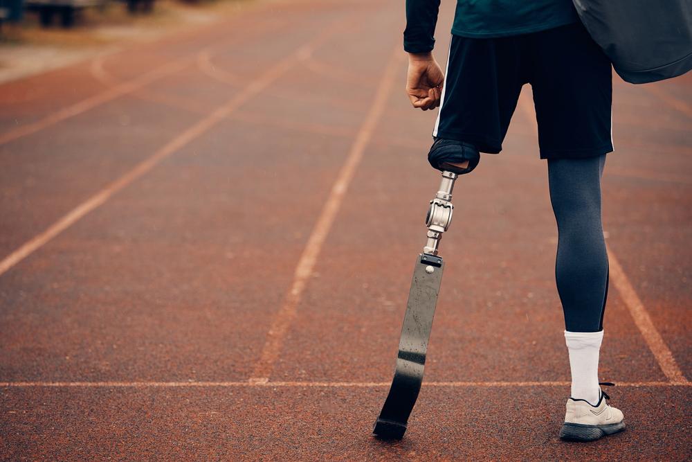 Young man with single leg prosthetic standing on track holding a bag.