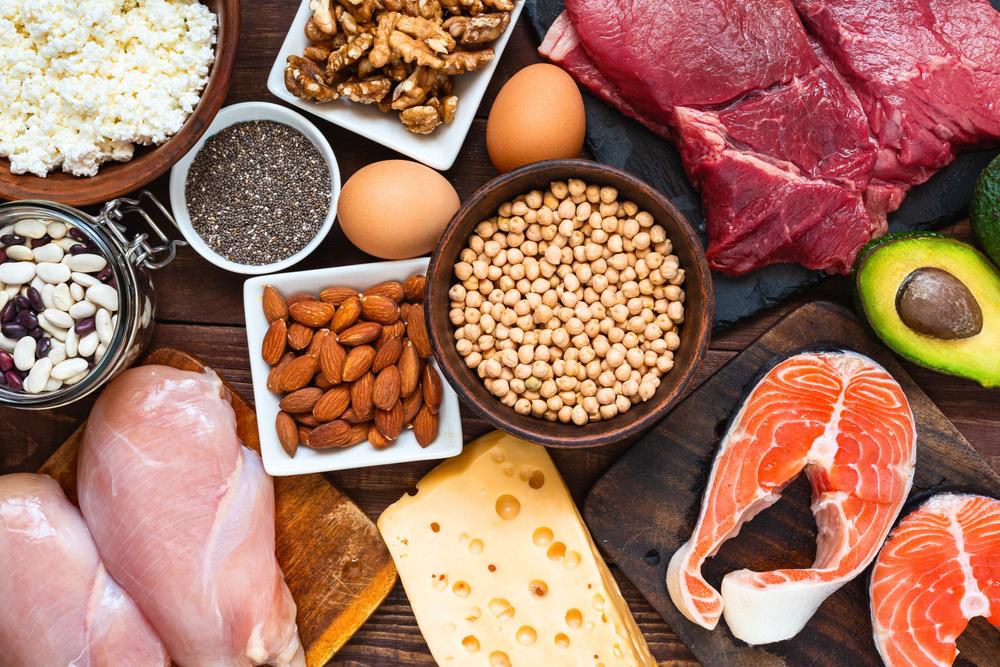 Protein rich foods on a table including meat, beans, nuts, and cheese.