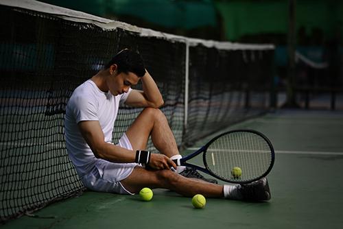 Male tennis player sitting against the net.