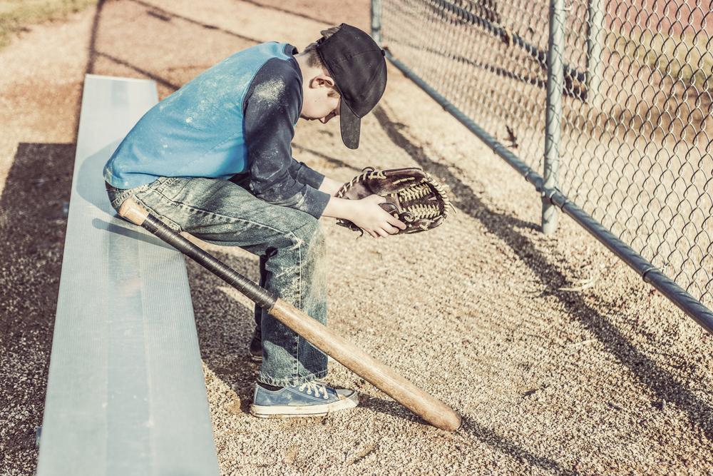 Young baseball player sitting alone on bench looking down.