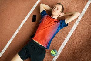 young man laying on track with eyes closed listening to music on phone.