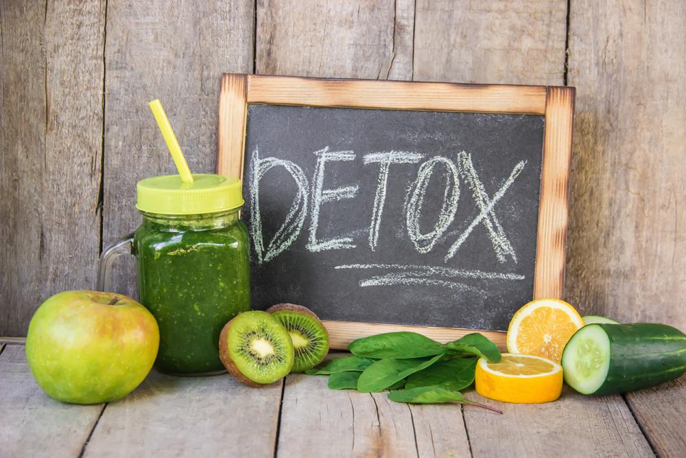 The word DETOX written on chalkboard next to fruits and veggies and juice.