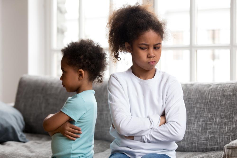 Young siblings angry at each other on couch.