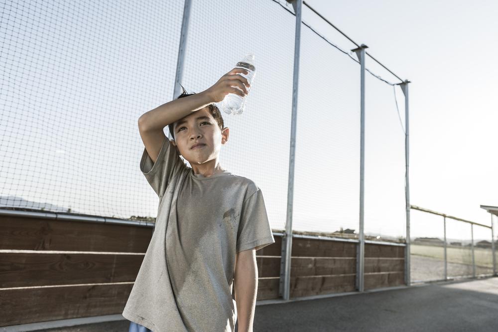 Young boy sweating and holding a water bottle in summer.