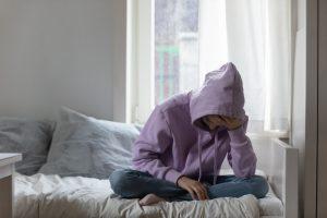 Young teen in hoodie sad on bed.
