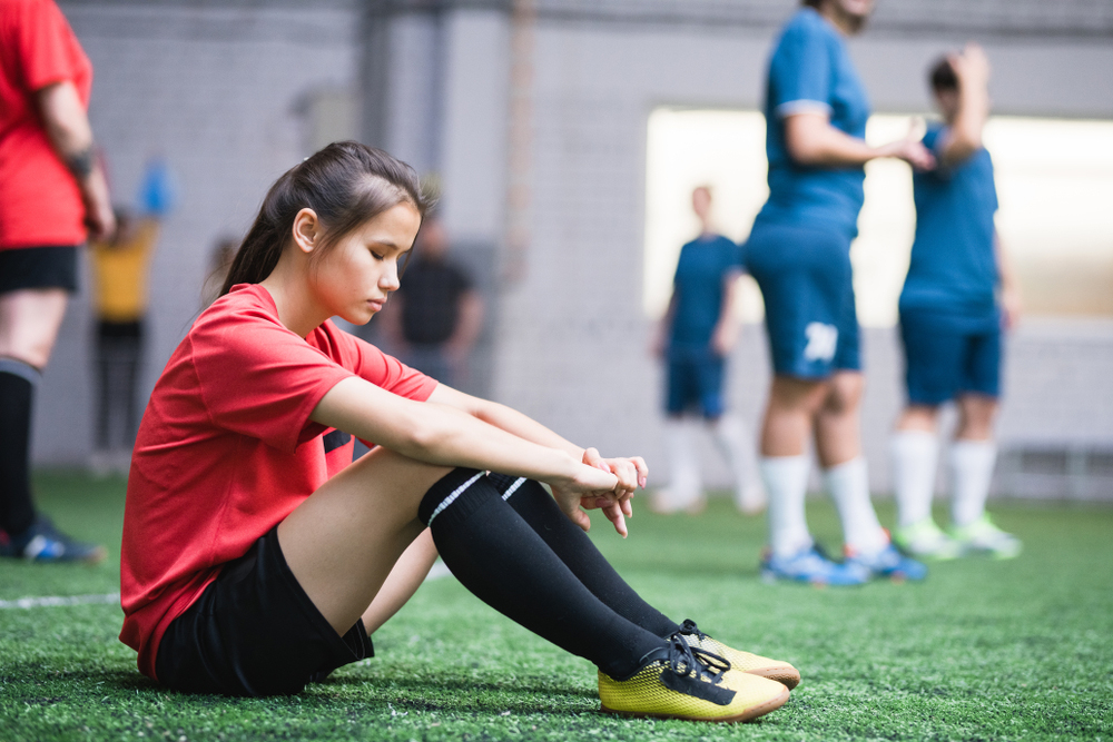Young female soccer playing sitting and looking upset.