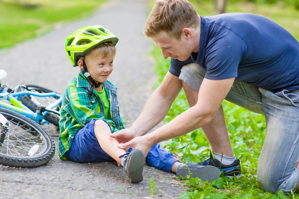 Dad helping son who hurt leg after falling off bike.