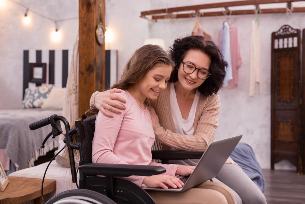 A mother with her daughter in a wheelchair looking at a laptop together.