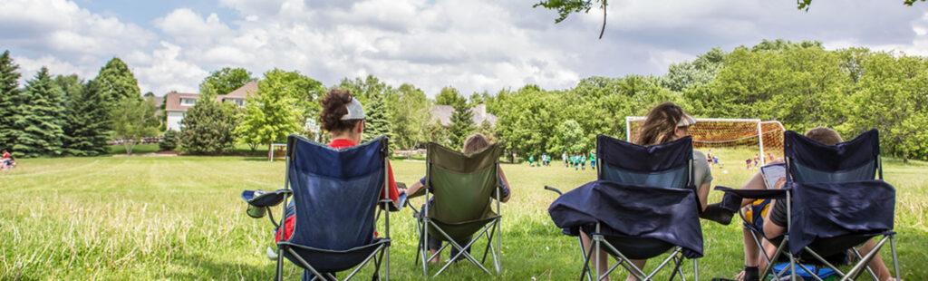 Parents sitting on sidelines of youth sports game outdoors.