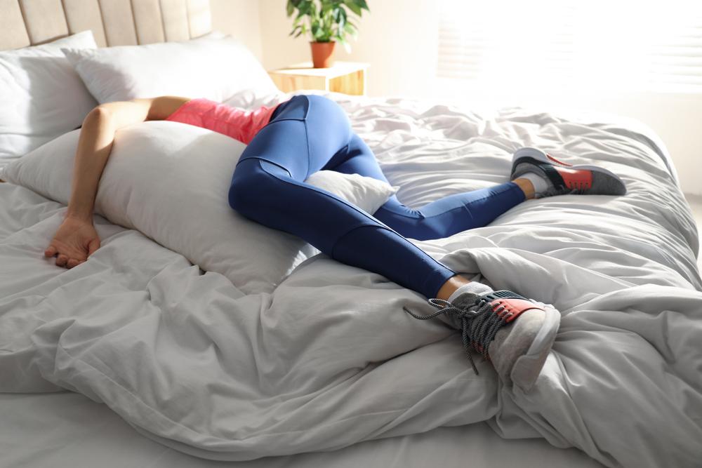Woman in workout gear with shoes laying in bed.