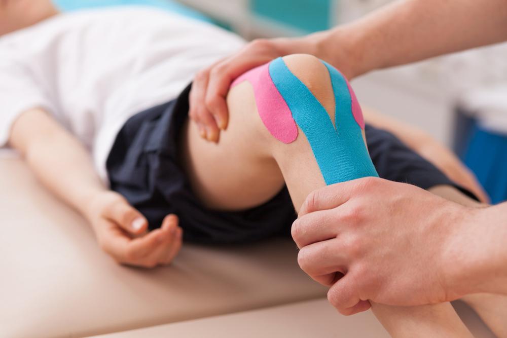 Kid with tape on his knee getting physical therapy.