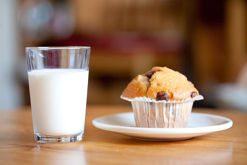 Muffin on a plate next to a cup of milk.