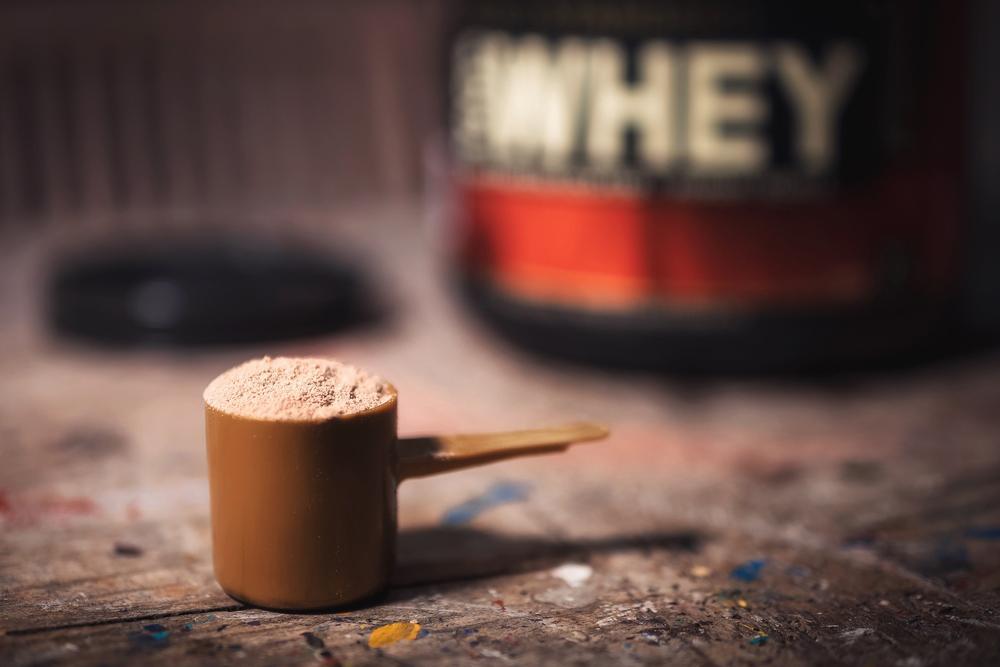 Cup of protein powder in front of a plastic tub that say "Whey."