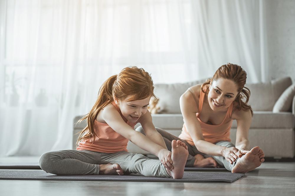 White mother and daughter stretching on mats in living room.