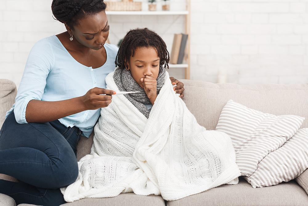 Black mother comforting sick child while looking at thermometer.