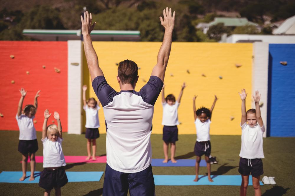 Man leading children in a yoga class outdoors.