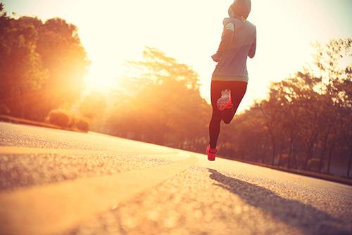 Young woman wearing a hoodie and running in the sun.