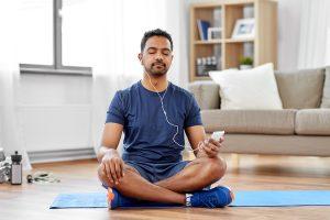 Adult man meditating while listening to headphones on yoga mat.