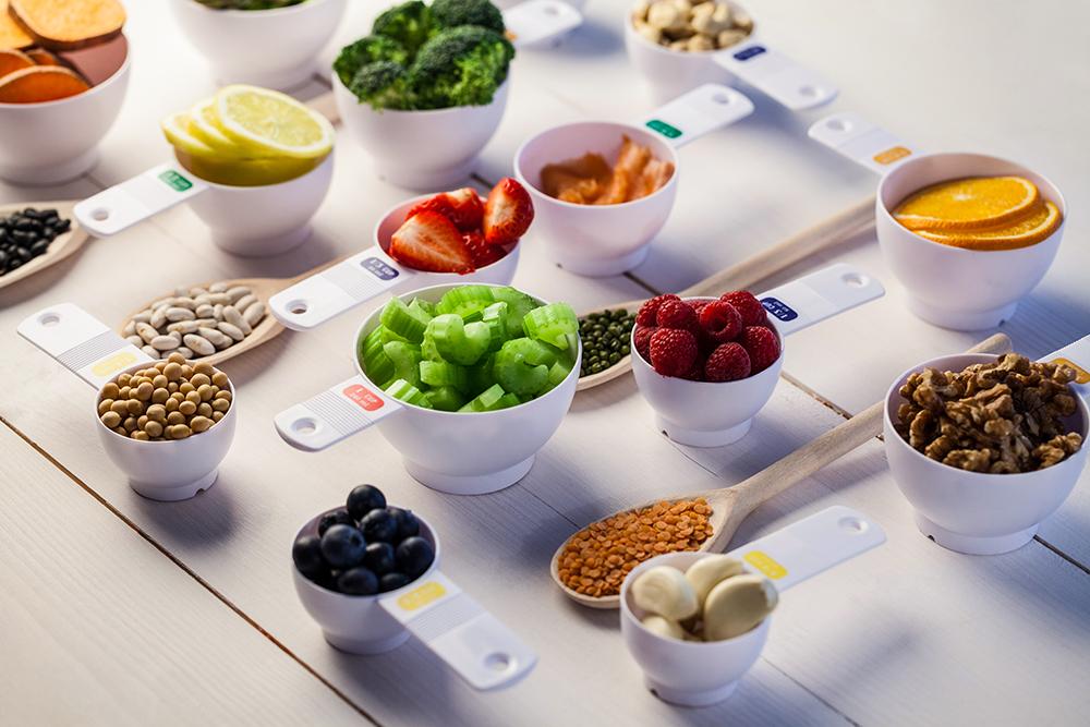 Measuring cups fullf of different fruits, nuts and veggies.