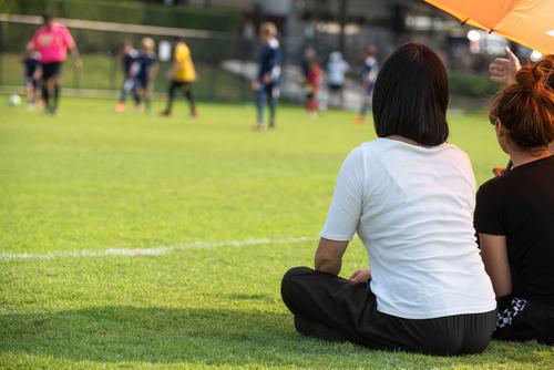 Two moms sitting on sidelines at youth soccer game.