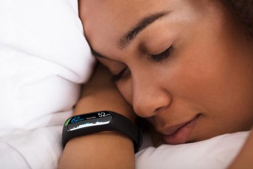 Young woman asleep in bed with sleep tracker on wrist.
