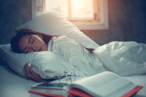 A young female teen sleeping next to a textbook in bed.