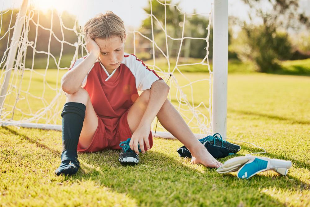 Young male soccer player sitting near goal upset.
