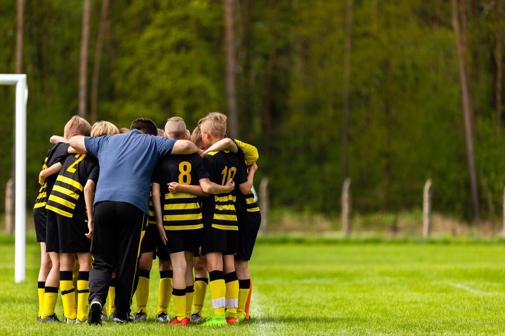 Young male soccer team huddling with coach.