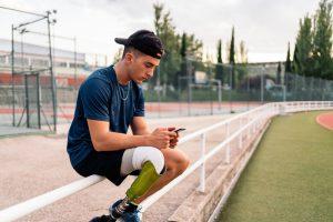 Young man with prosthetic leg on cell phone nex to a track.