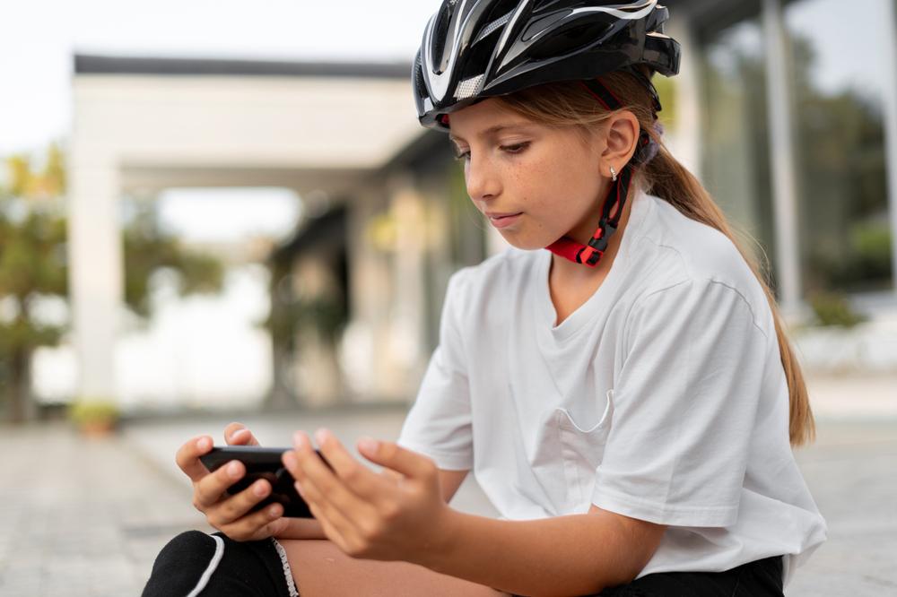 Young girl wearing helmet and knee pads on cell phone.