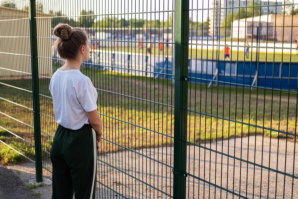 Young female athlete watching game behind a fence.