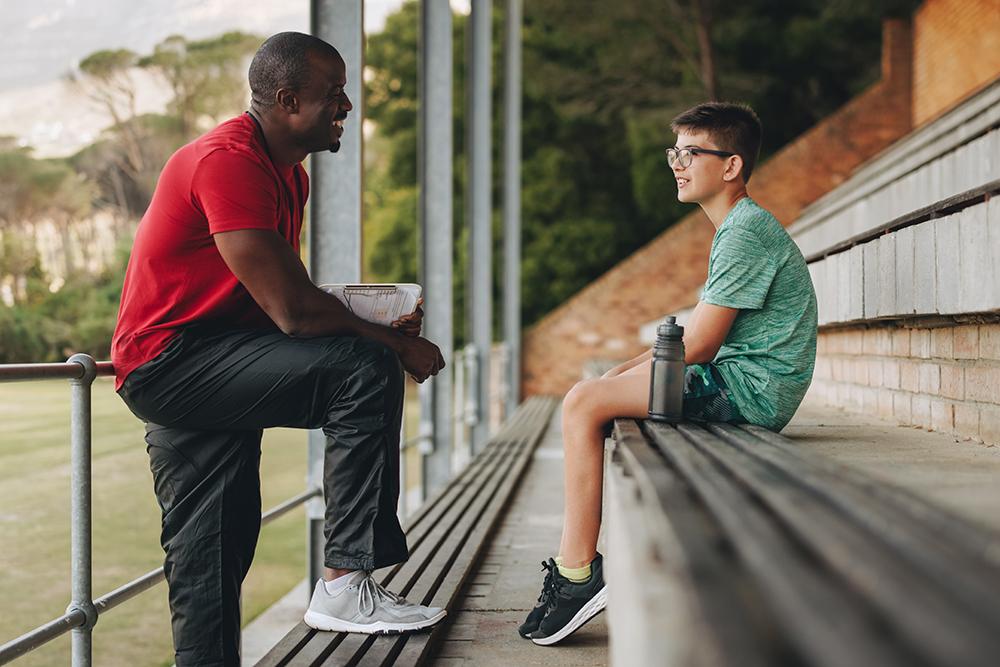 Coach talking to male athlete in bleachers.