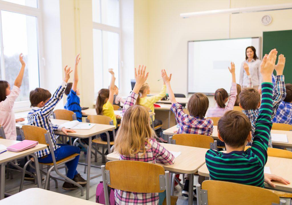 Students raising hands in a classroom.