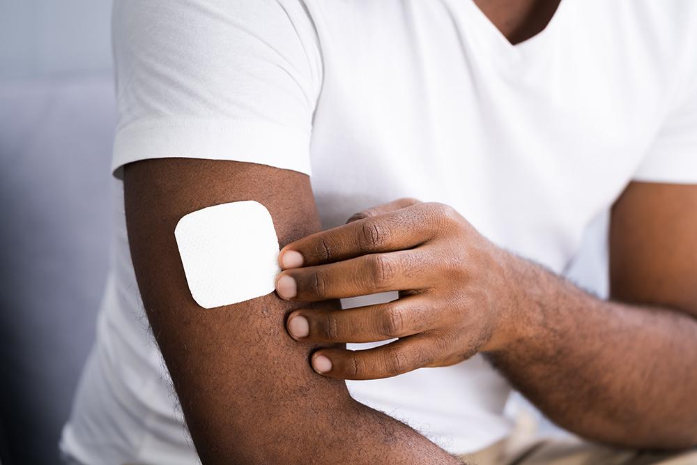 Young man putting a white patch on his bicep.