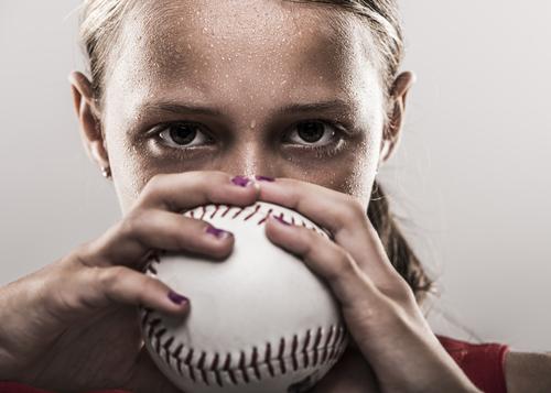 Young sweaty girl holding a softball.