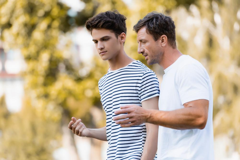 Father and teen son talking while walking outside.