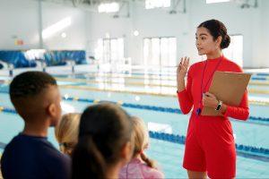 resources Female swim coach talking to young athletes next to indoor pool.
