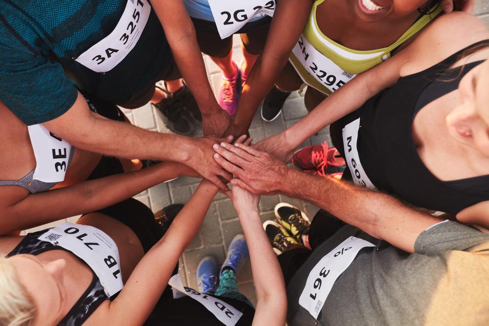 Diverse group of track athletes with hands in center together.