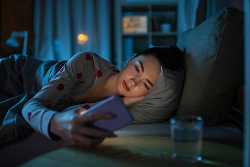 Young woman awake on phone in bed.