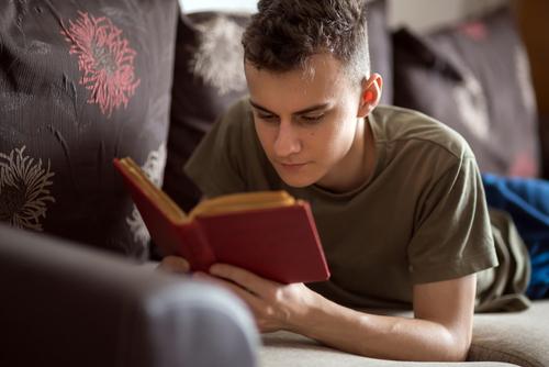 Teen boy reading book on couch.