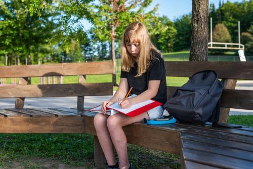 Teen girl writing on notebook on park bench.