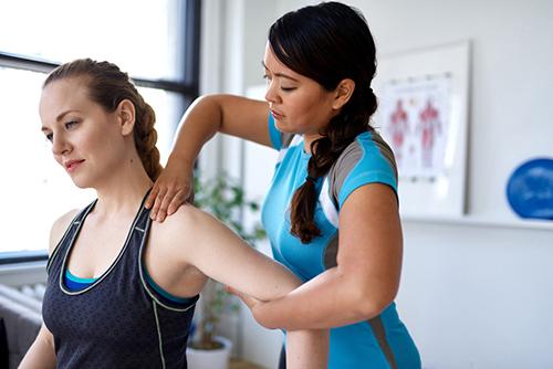 Young trainer massaging shoulder of female athlete.