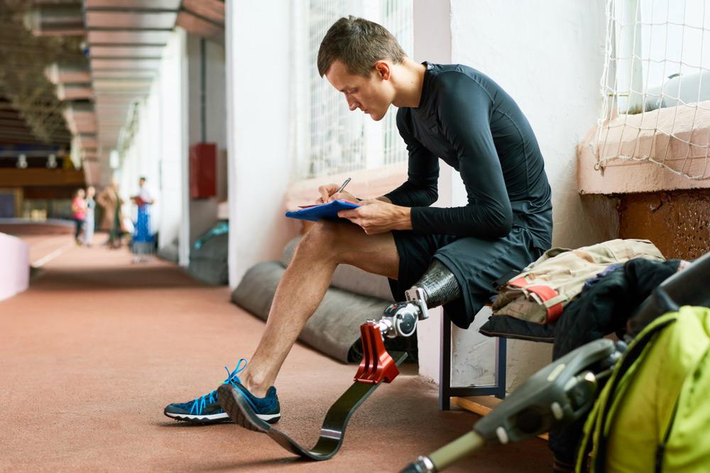 Male athlete with leg prosthetic sitting on bench writing on paper.