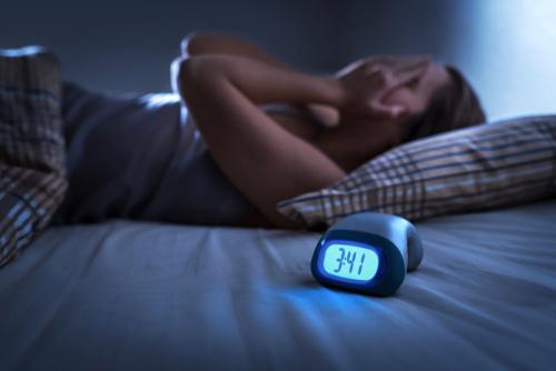 Woman awake in bed with a clock that reads 3:41 a.m.