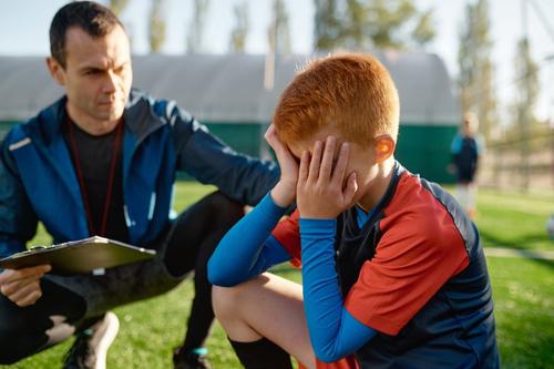 Young boy being comforted by coach on soccer field.