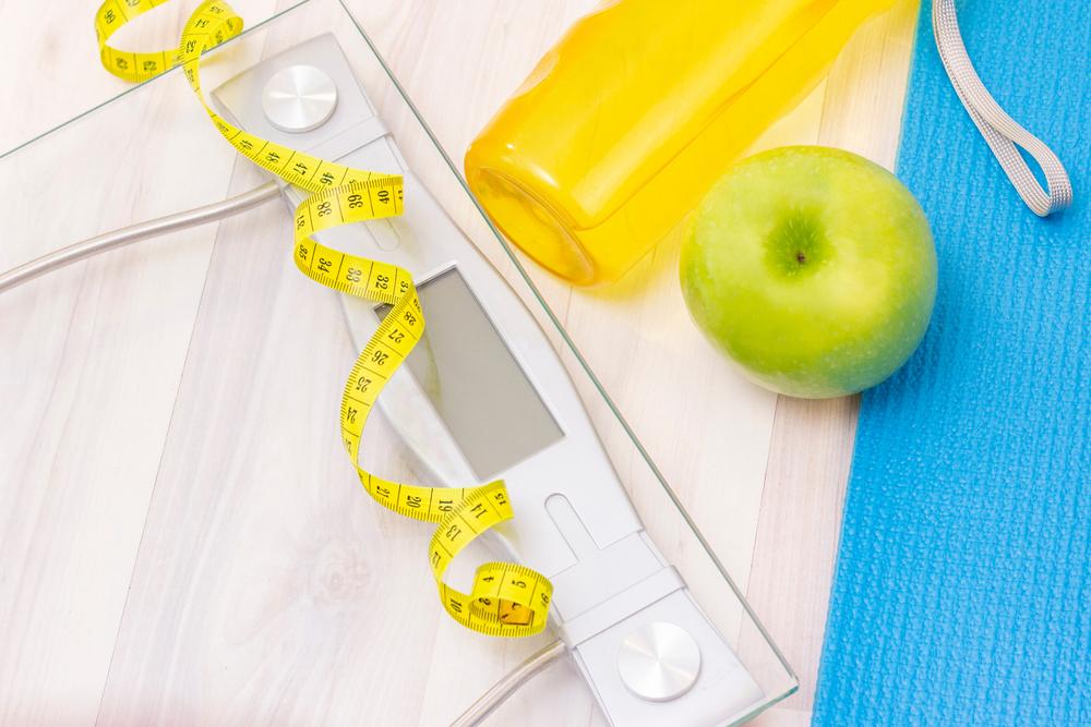 A scale next to a measuring tape, water bottle, and apple.