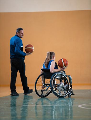 Young, female wheelchair basketball athlete next to coach.